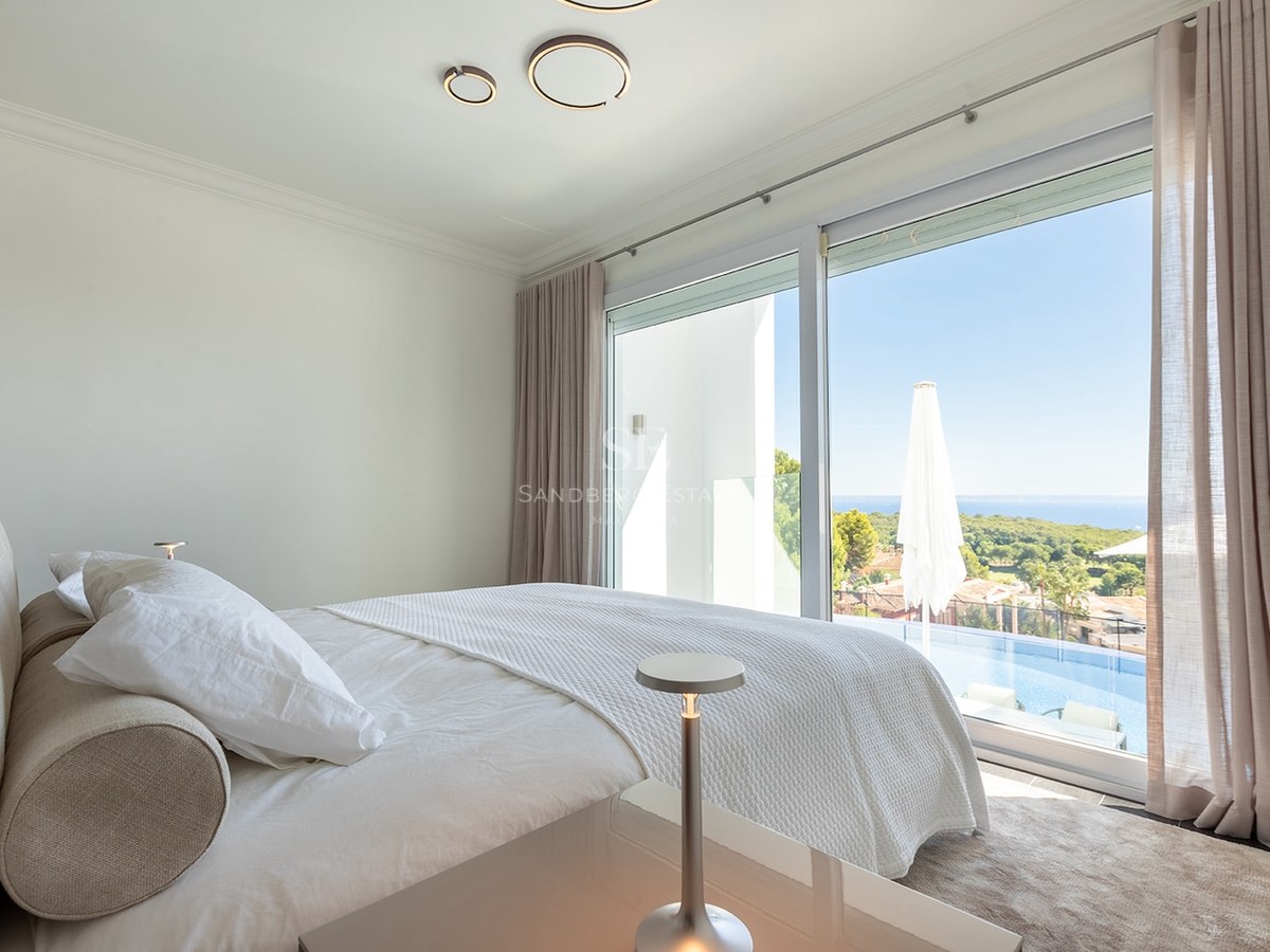 Modern bedroom with white bedding, large windows overlooking a private infinity pool and distant sea view.
