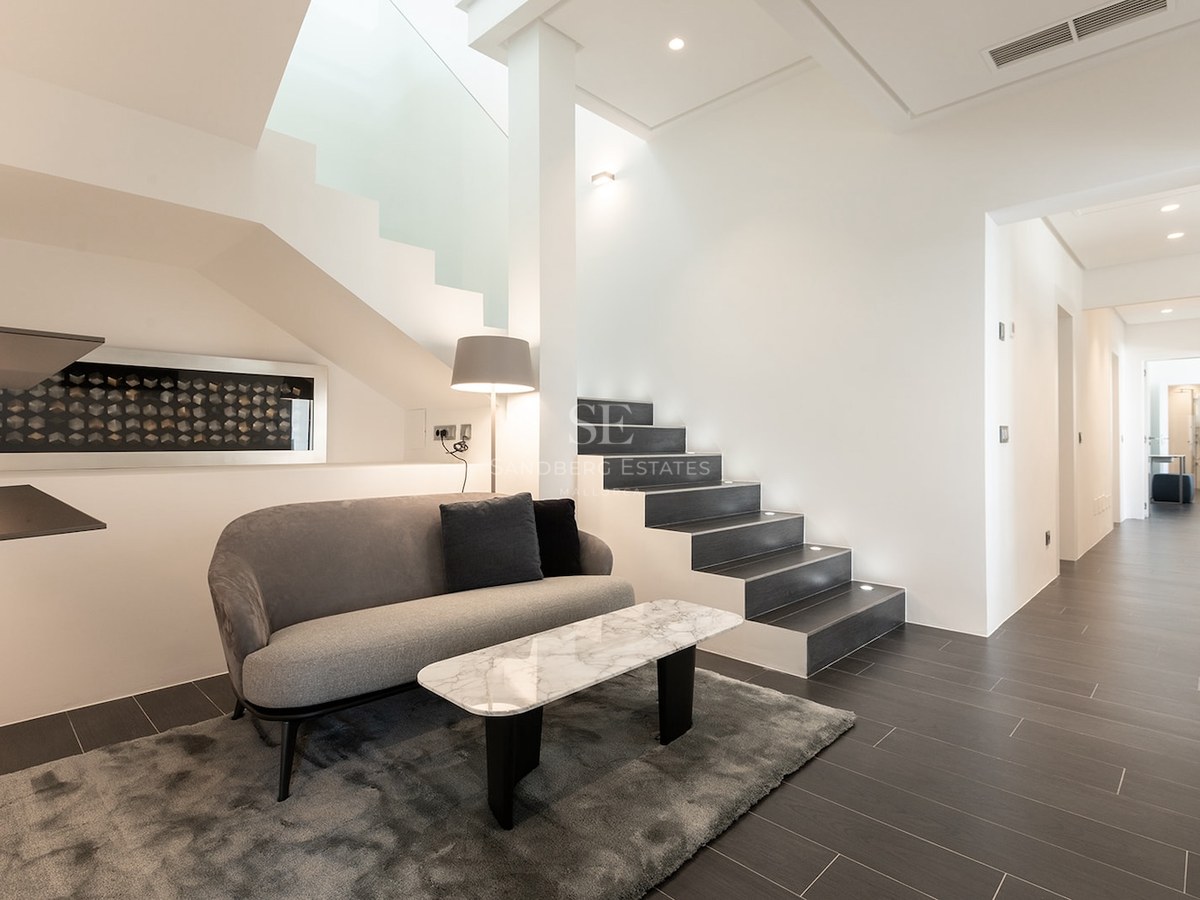 Modern lounge area featuring a grey sofa, marble table, and a contemporary dark-tread staircase with integrated lighting.