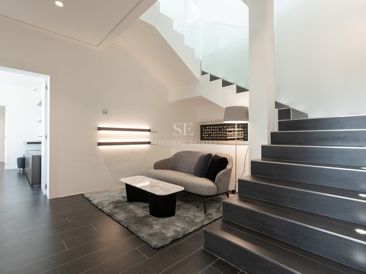 Modern interior featuring dark stairs with integrated LED lighting, a gray sofa, and a marble coffee table.