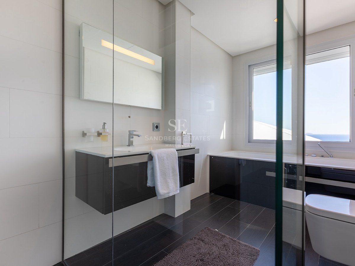 Modern bathroom with white tiled walls, dark floors, a floating vanity, and a bathtub under a large window.