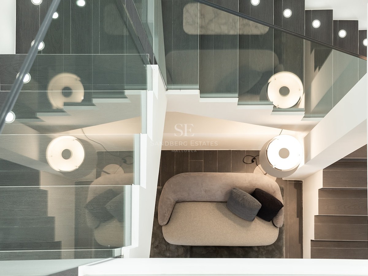 Overhead view of a staircase with glass railings looking down onto a grey sofa and a designer lamp.