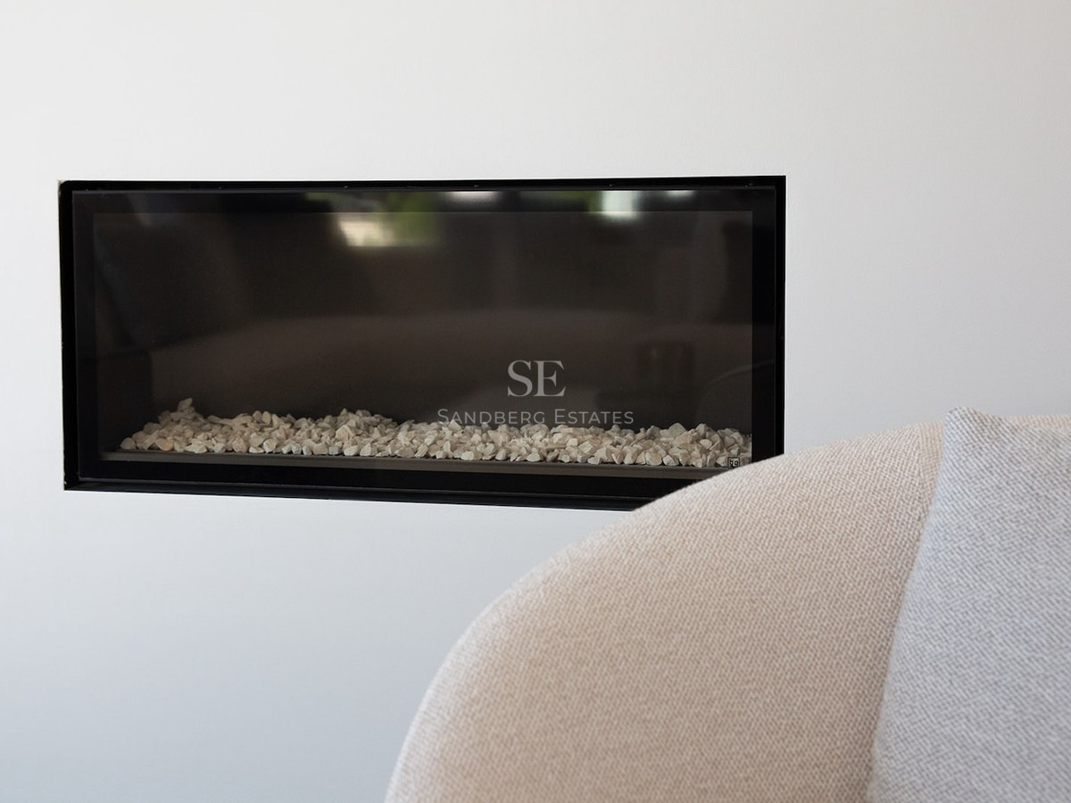 Close-up of a rectangular black-framed fireplace built into a white wall with white stones inside.