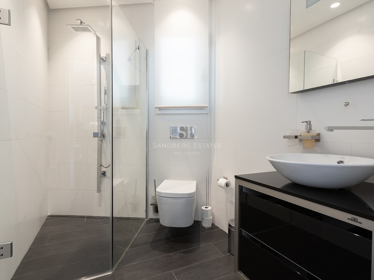 Contemporary bathroom featuring white tiles, walk-in glass shower, wall-mounted toilet, and vessel sink on black vanity.