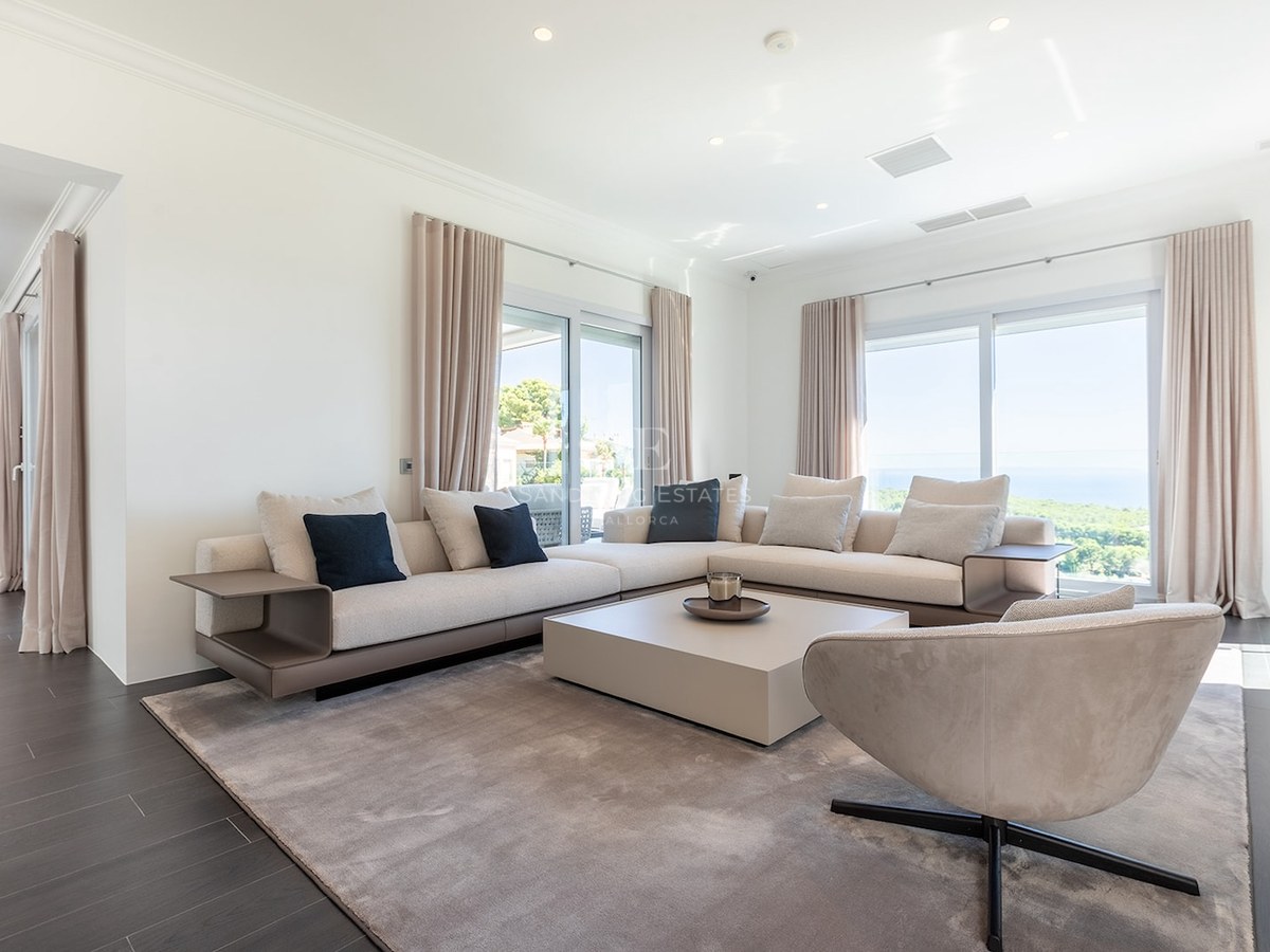 Spacious white living room with beige sectional sofa, designer armchair, and large windows overlooking the ocean.