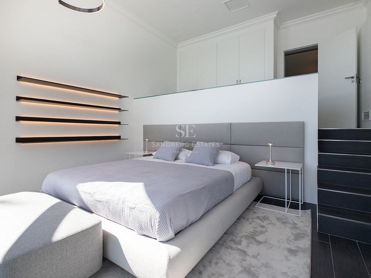 Modern bedroom featuring a gray bed, integrated LED wall shelving, and minimalist white interior.