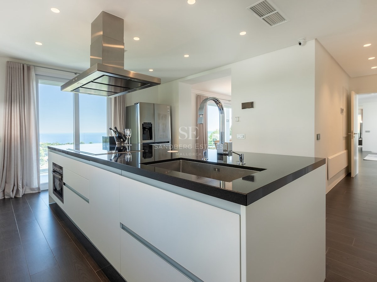Modern kitchen featuring a black island, stainless steel hood, and floor-to-ceiling windows with a sea view.