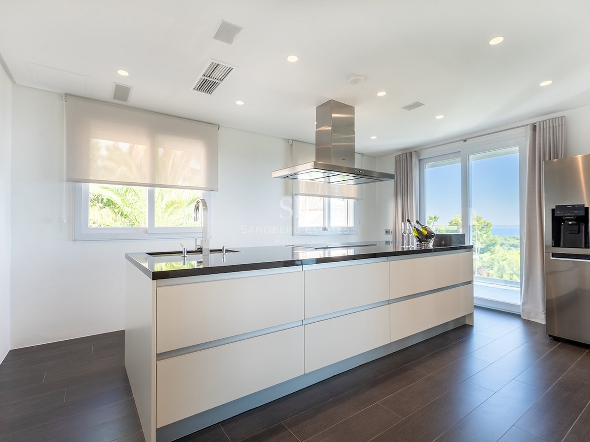 Bright modern kitchen featuring a large white island with black countertop, stainless steel appliances, and sea views.
