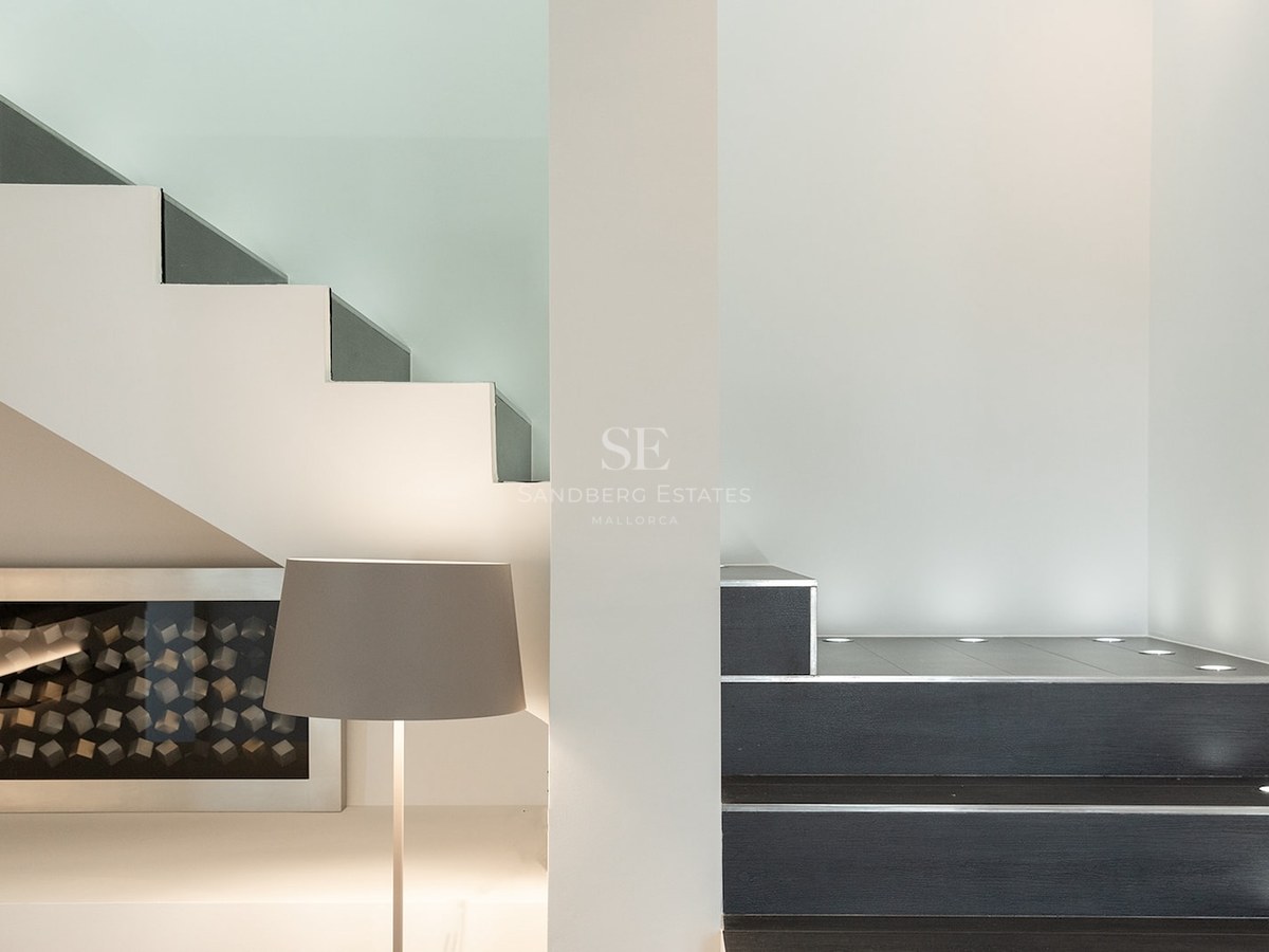 Close-up of a minimalist staircase with dark steps, white walls, and circular recessed floor lights.