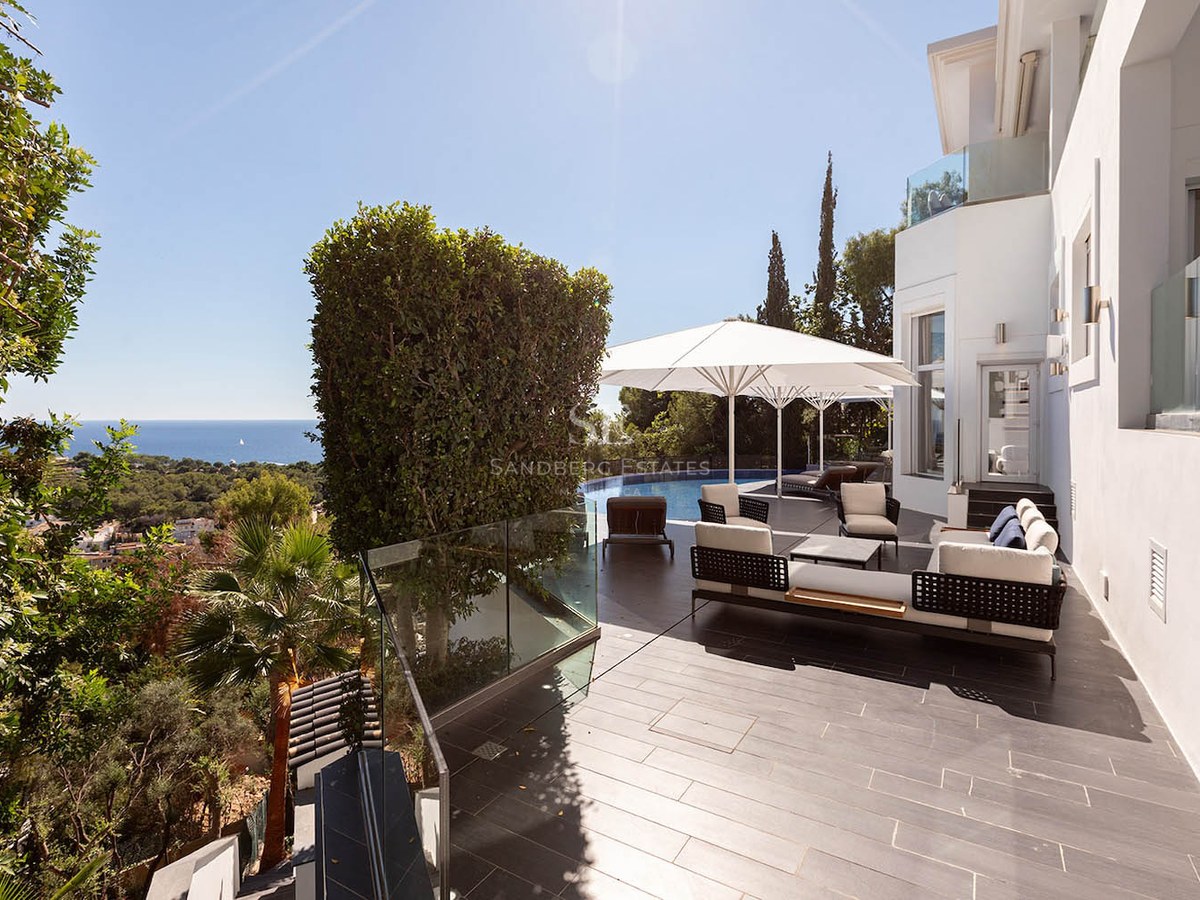 Modern terrace with designer lounge furniture, white umbrellas, and an infinity pool overlooking the sea.