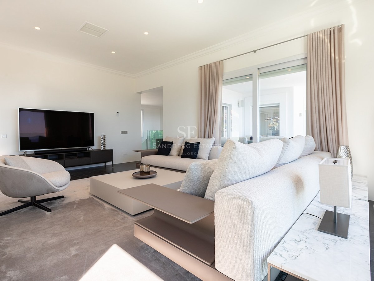 Contemporary living room featuring a large beige sofa, a designer armchair, and a flat-screen TV in a bright space.