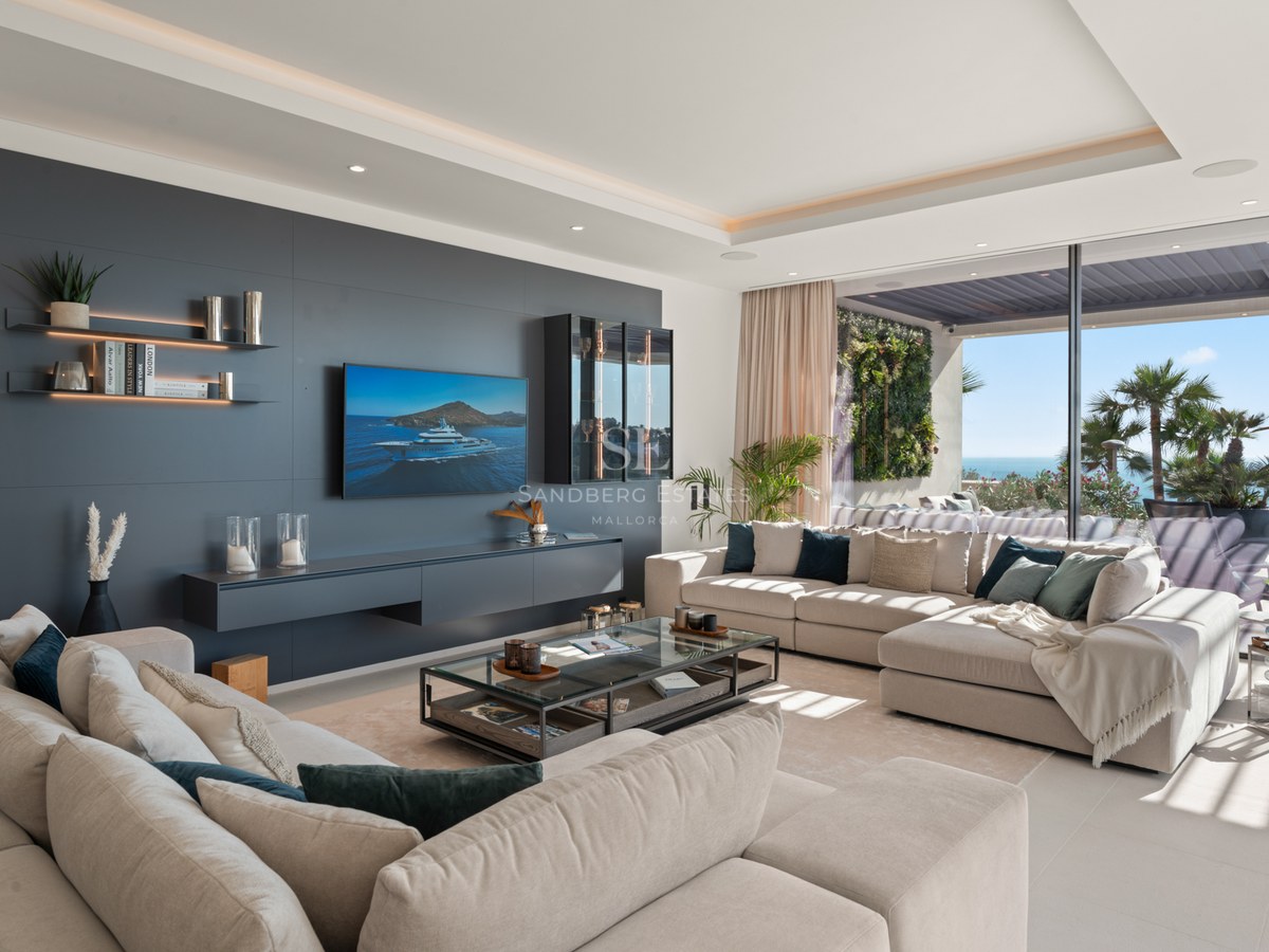 Bright living room with large beige sofas, charcoal accent wall, TV, and panoramic glass doors opening to a sea view terrace.