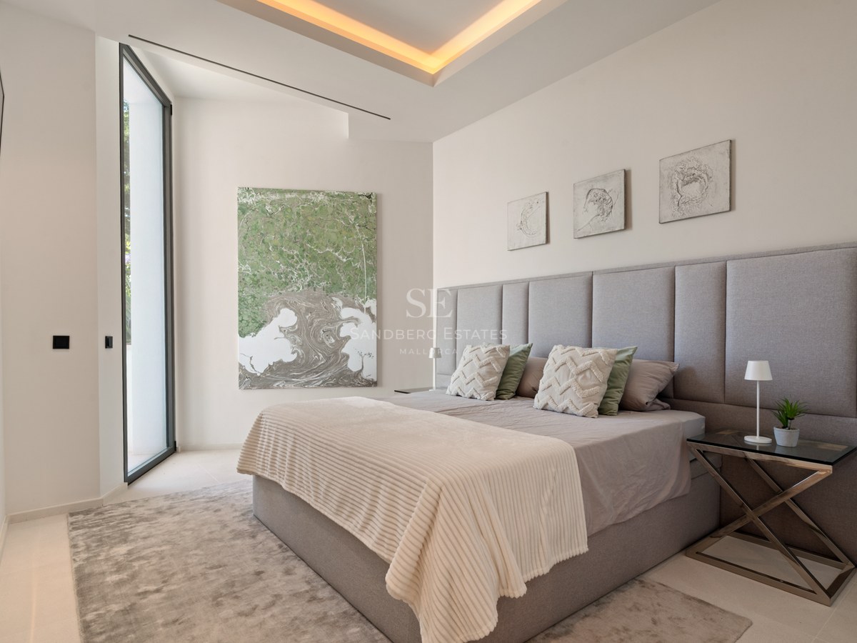 Bedroom with grey upholstered headboard, king-size bed, abstract art, and warm recessed lighting.