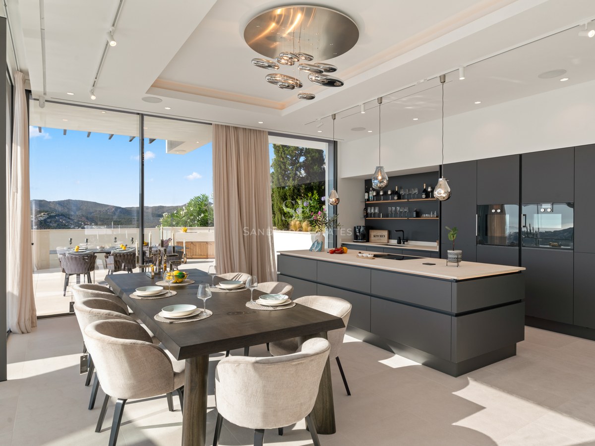 Modern kitchen with large grey island and wooden dining table next to floor-to-ceiling windows with mountain views.