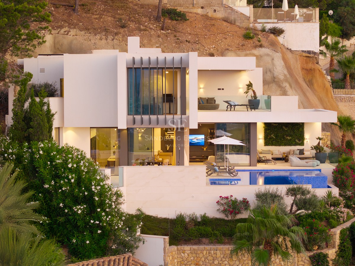 Modern white multi-level villa with a swimming pool, terraces, and large glass windows built into a rocky hillside.