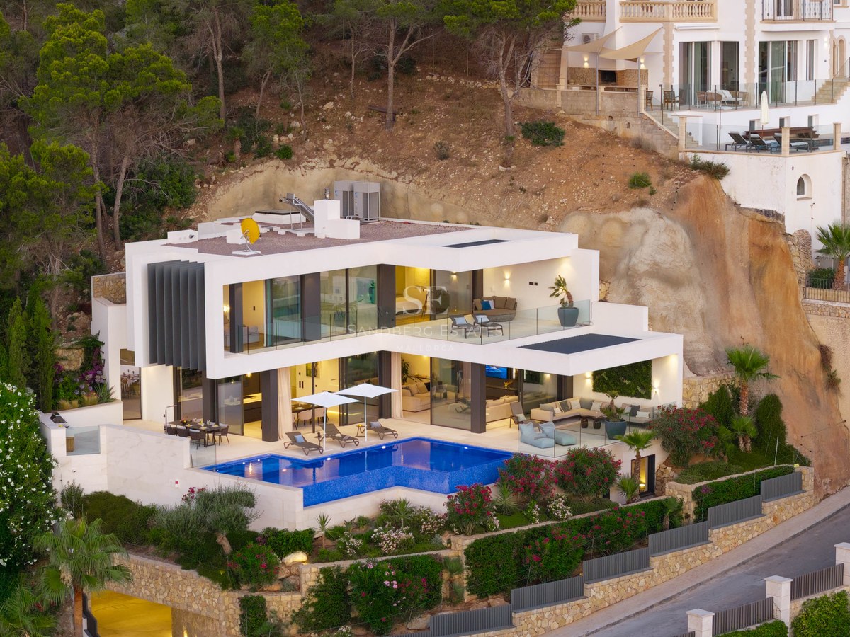 Modern white villa on a hillside featuring a bright blue swimming pool and glass-walled terraces.