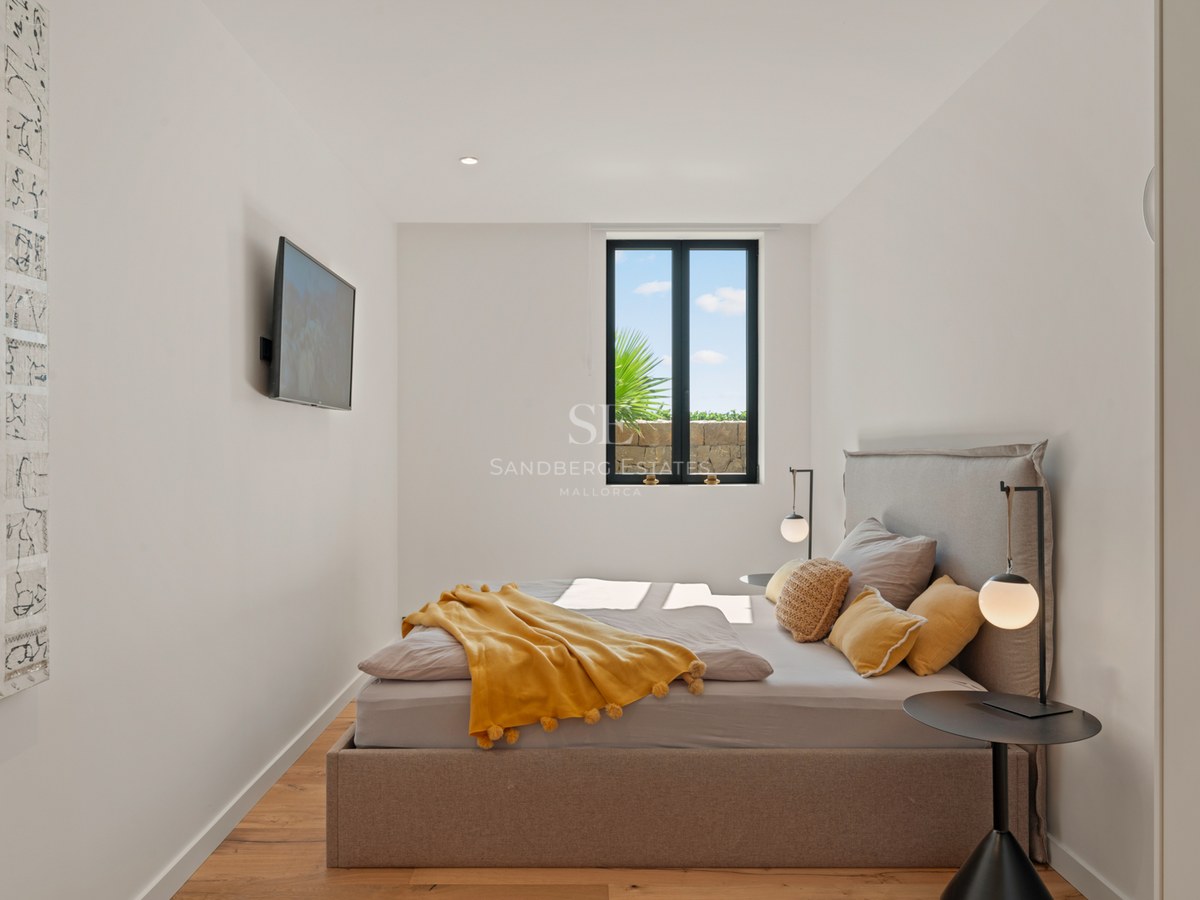 Bright bedroom featuring a taupe upholstered bed, yellow pom-pom blanket, minimalist lamps, and a scenic window view.