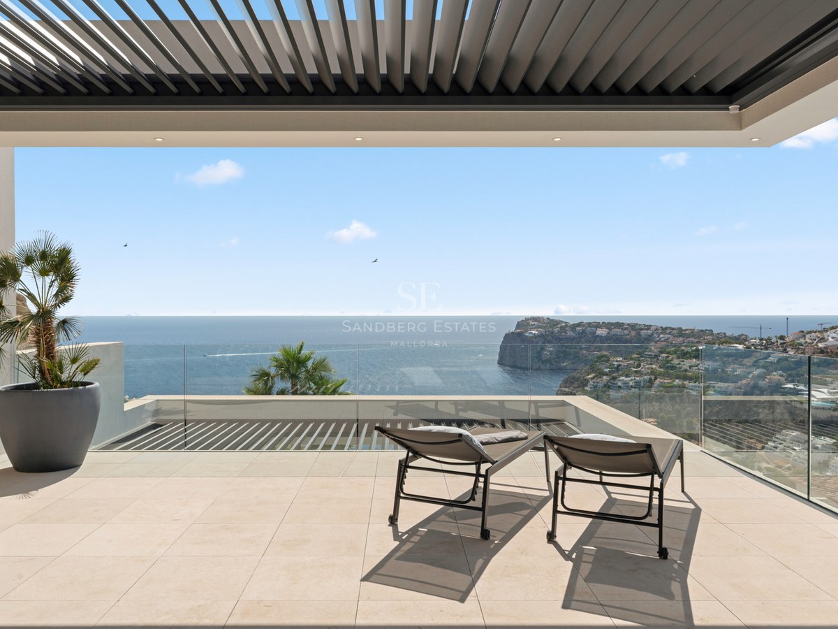Modern terrace with glass railings, two sun loungers, and a wide view of the ocean and coastal cliffs.