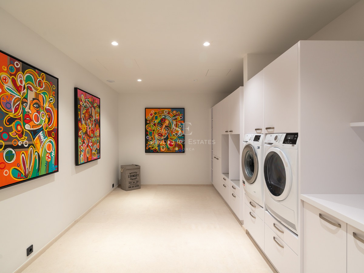 Modern white laundry room with washer, dryer, minimalist cabinetry, and three vibrant colorful pop-art portraits.