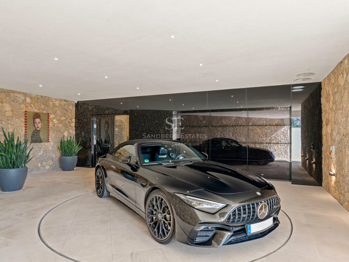 A black Mercedes sports car on a circular rotating platform in a modern garage with natural stone walls and mirrors.