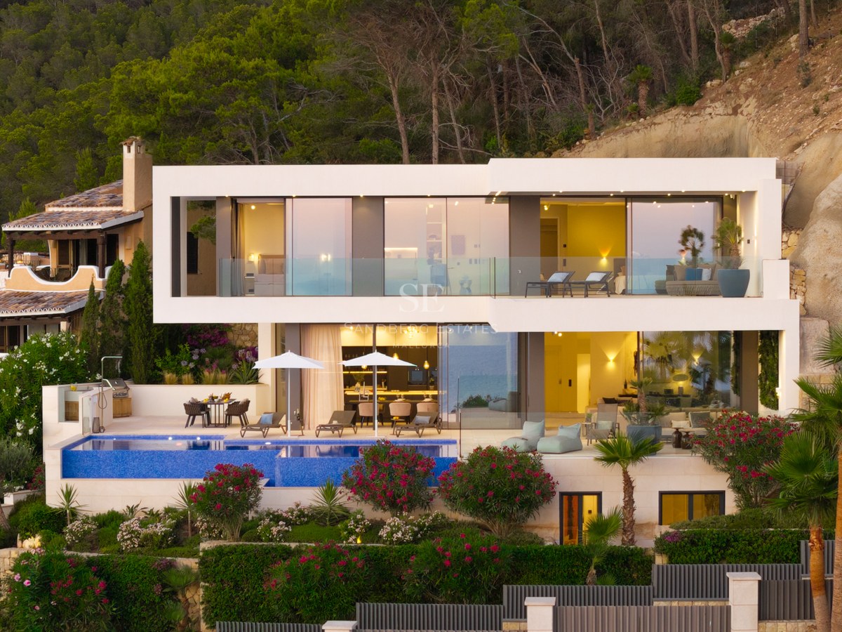 Facade of a modern white two-story villa with an infinity pool and large glass windows at dusk.