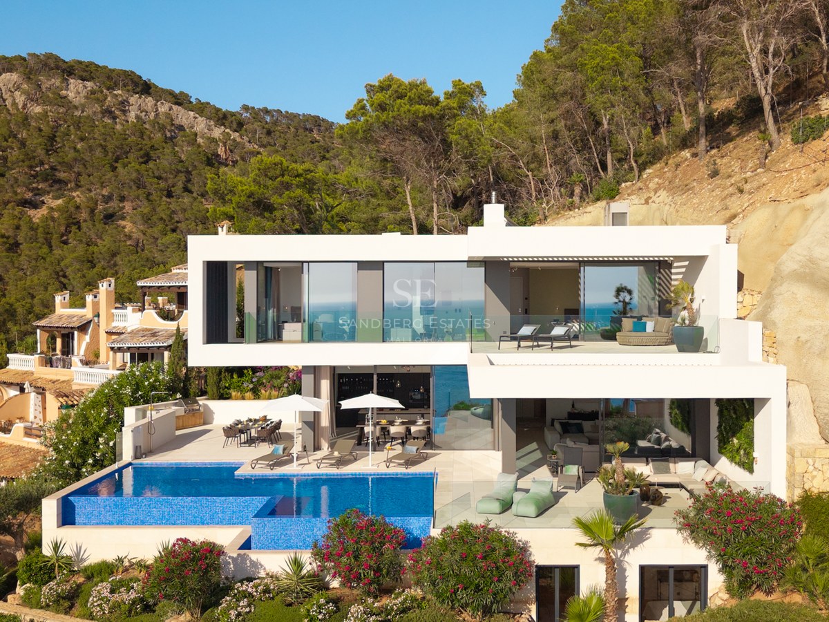Multi-level modern white villa on a hillside featuring a large infinity pool, lounge terraces, and lush greenery.
