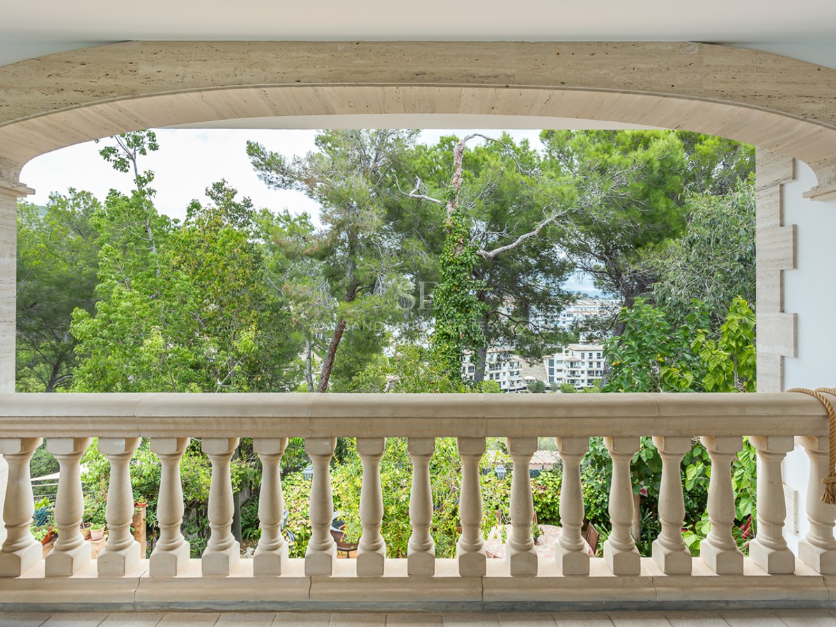 A beige stone balustrade under a wide stone arch overlooking lush green trees and distant buildings.