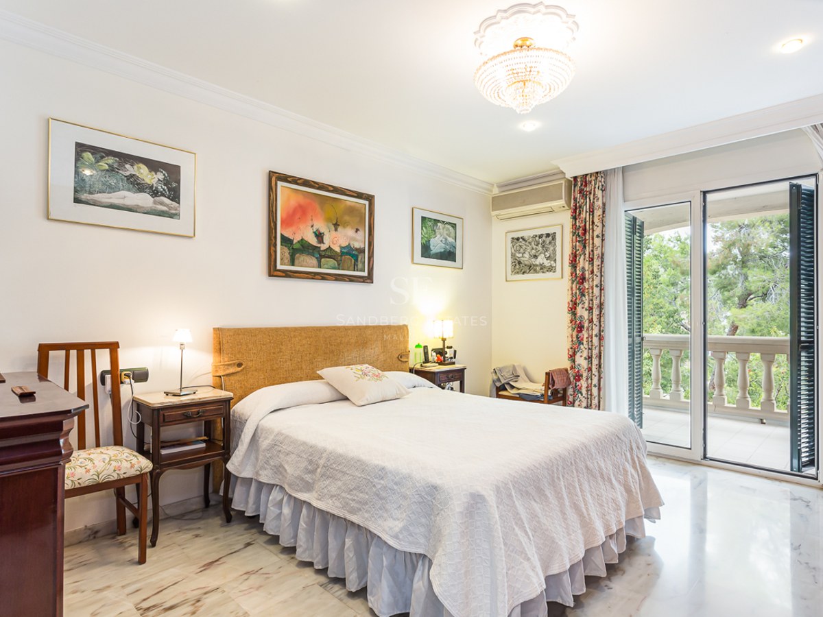 Elegant bedroom with a double bed, marble flooring, crystal chandelier, and glass doors opening to a balcony.