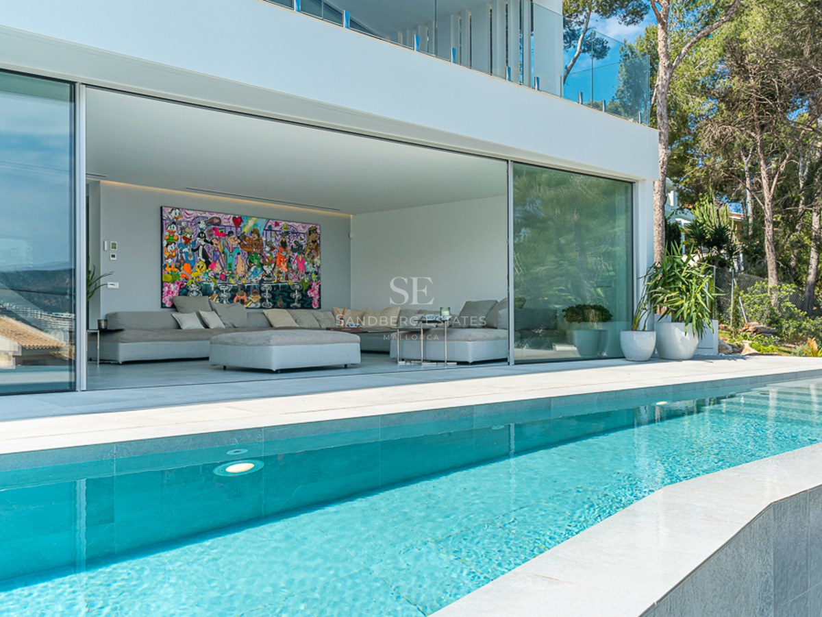 A crystal-clear pool in front of a modern open-plan living room with large glass sliding doors and pop art.