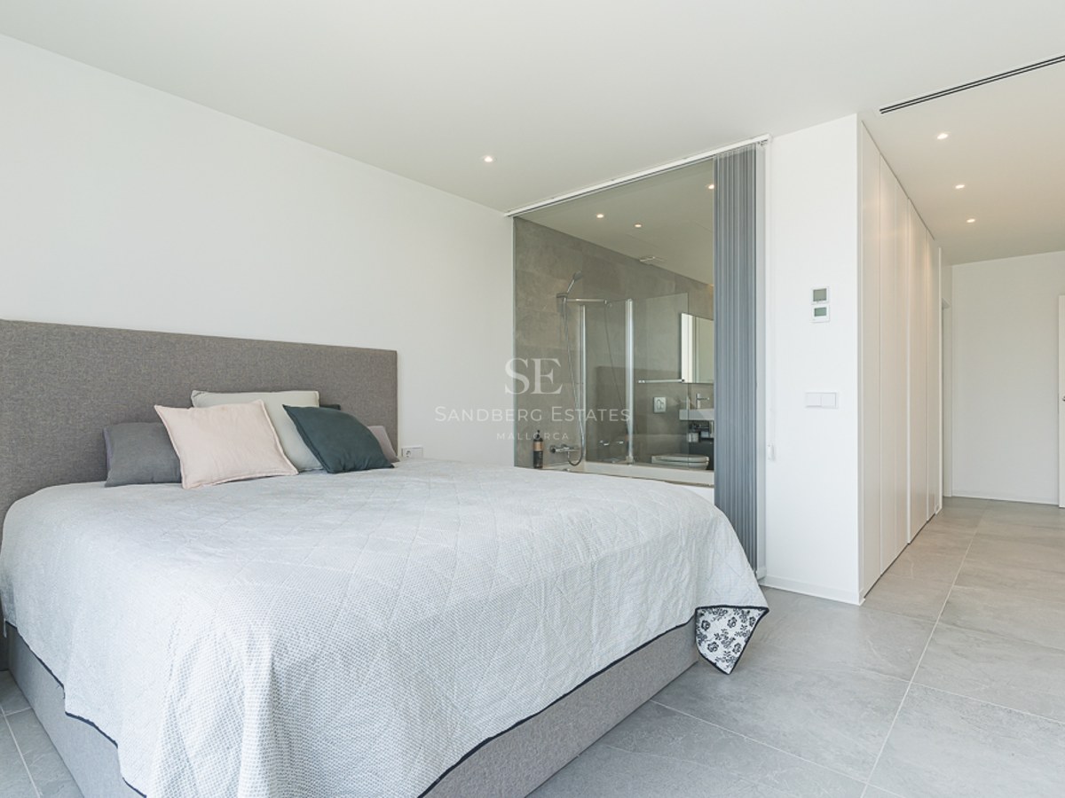 Minimalist master bedroom with a large bed and a glass-enclosed ensuite bathroom featuring a walk-in shower.