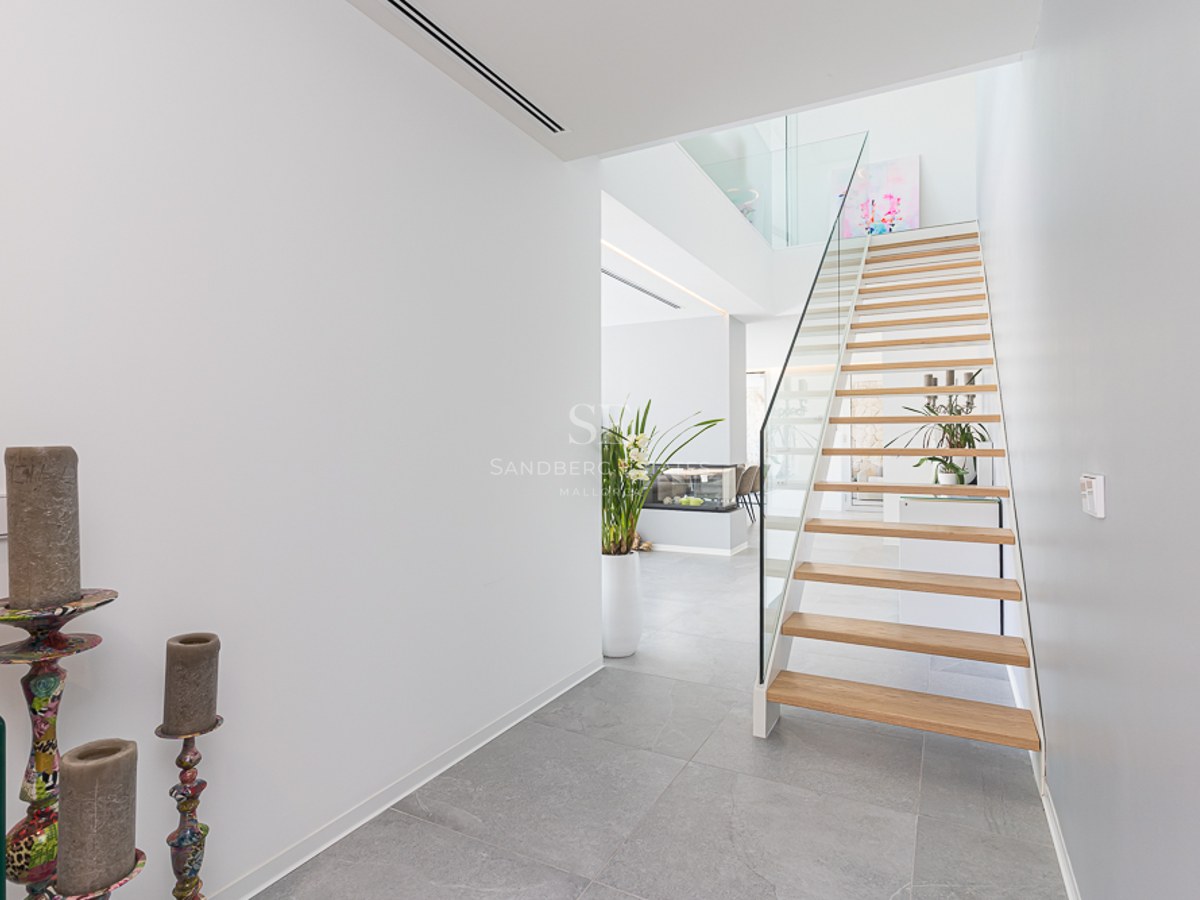 Bright modern hallway featuring a light wood floating staircase with glass railings and grey stone flooring.