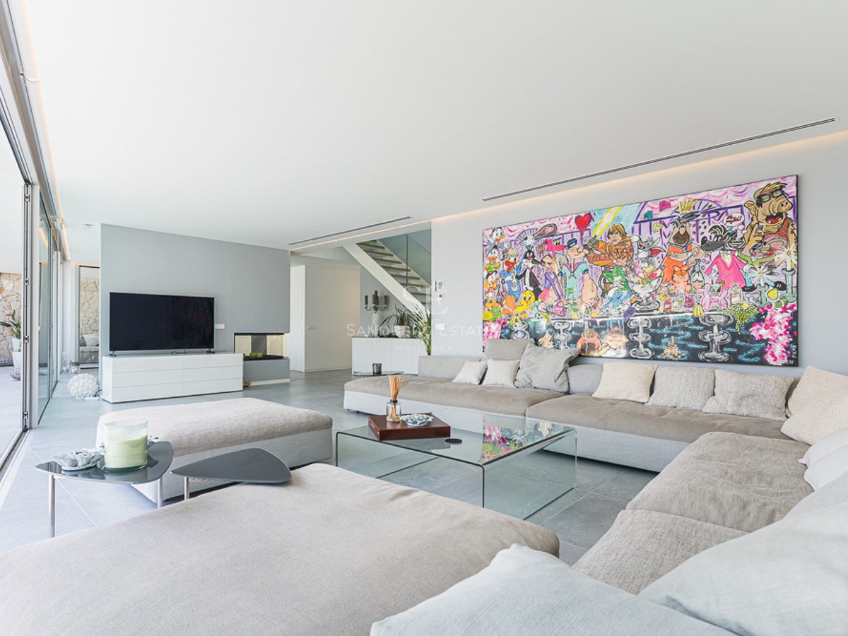 Modern living room with large beige sofa, glass table, and a massive colorful cartoon painting on a white wall.