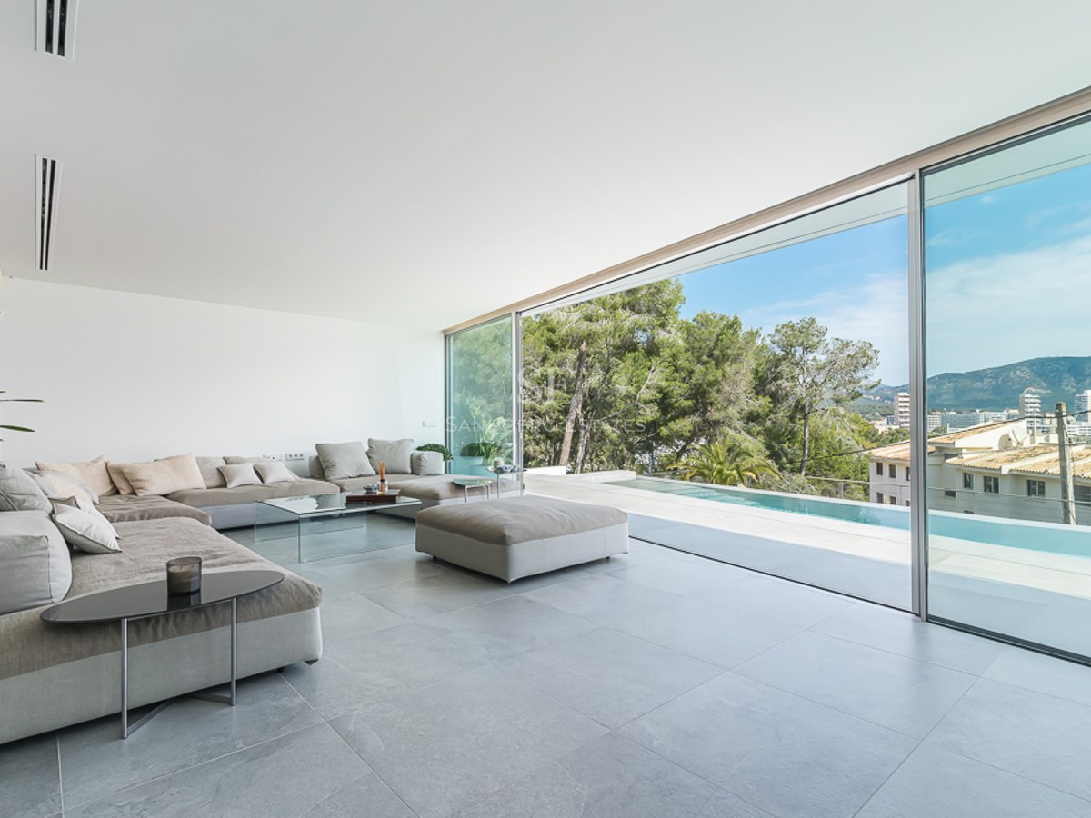 Spacious minimalist living room with grey sectional sofas and floor-to-ceiling glass doors overlooking a pool and mountains.