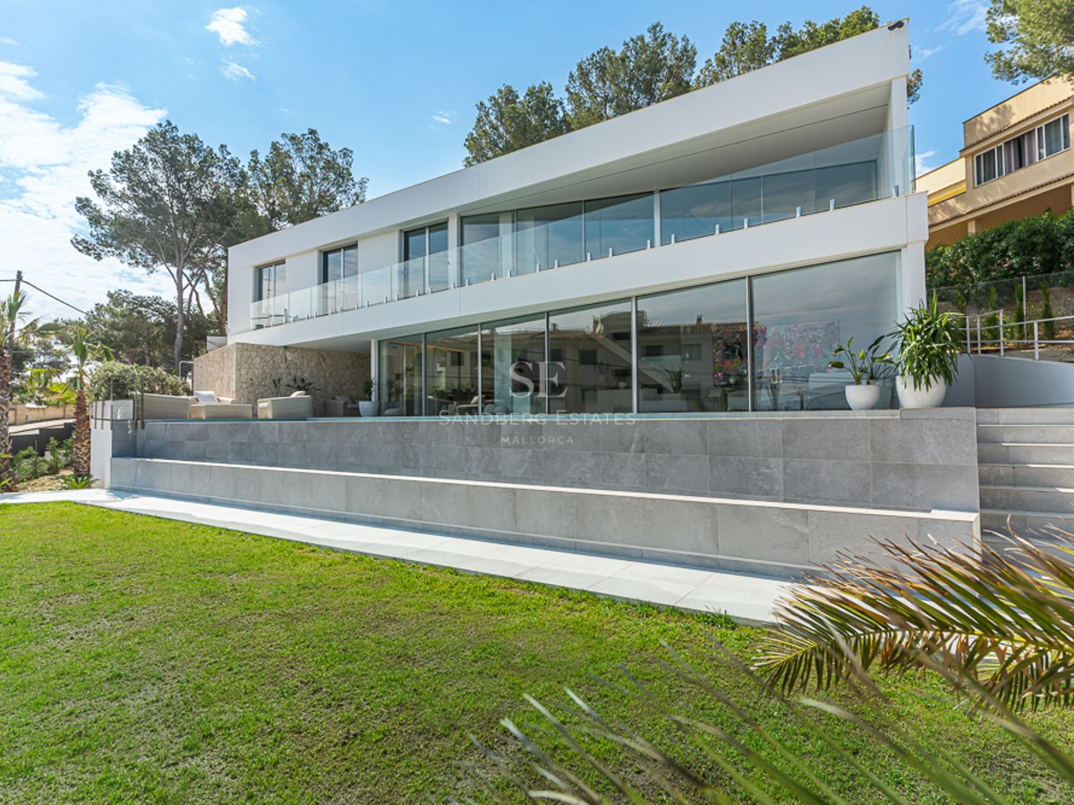 White modern villa with large windows, infinity pool, and green lawn under a sunny sky.