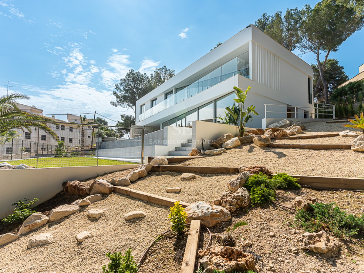 Side view of a modern two-story white villa with large glass windows and a tiered rock garden with gravel.