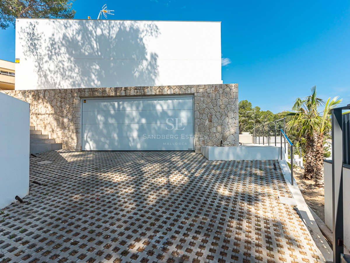 Modern white garage door in a natural stone wall with patterned pavers and palm trees.