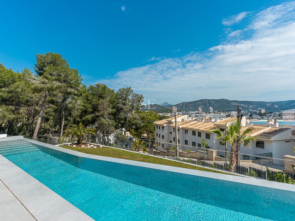 Luxury infinity swimming pool with stone tiling, overlooking a coastal town, mountains, and the sea under a clear blue sky.