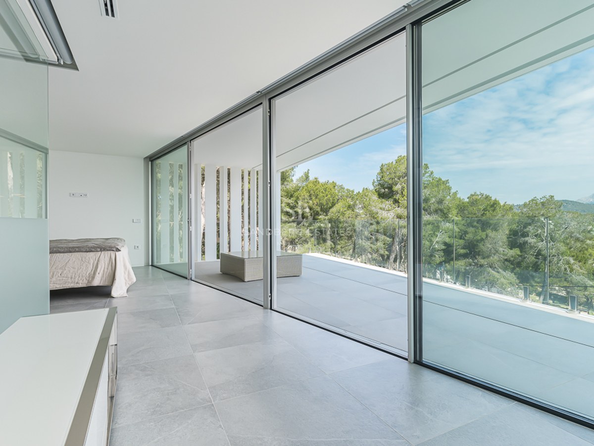 Bright minimalist bedroom with large sliding glass doors opening to a terrace with forest views.