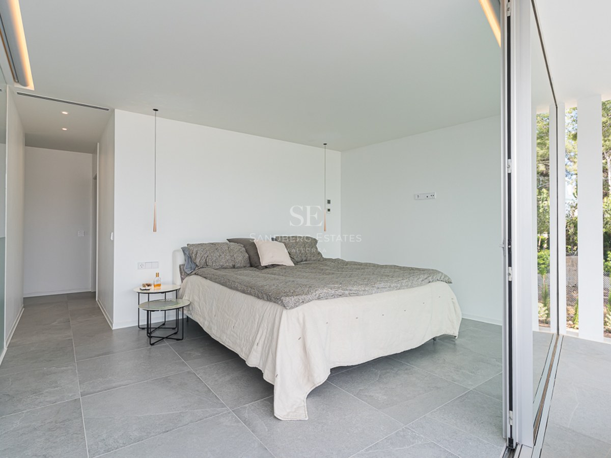 Minimalist bedroom with grey stone floors, white walls, and a large sliding glass door opening to a garden.
