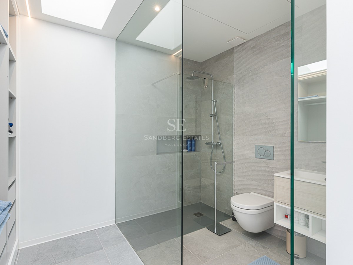 Minimalist bathroom featuring grey stone tiles, a glass walk-in shower, wall-hung toilet, and a bright skylight.
