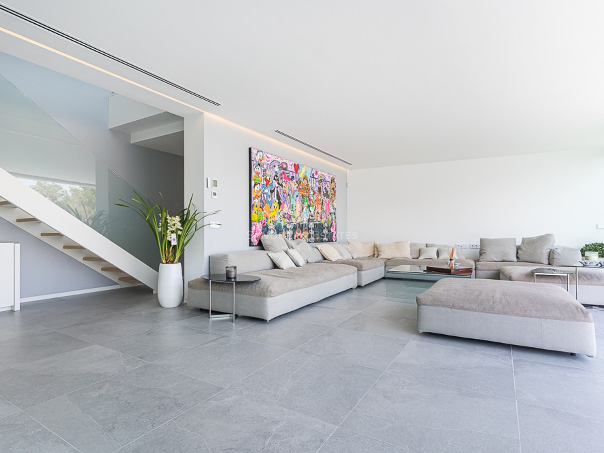 Spacious living room with large grey modular sofa, colorful wall art, and glass-railing staircase.