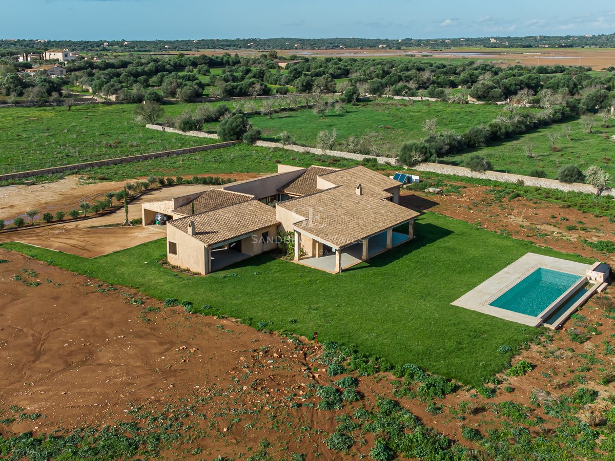 Bird's eye view of a sand-colored modern villa with a turquoise pool and large lawn in a rural landscape.