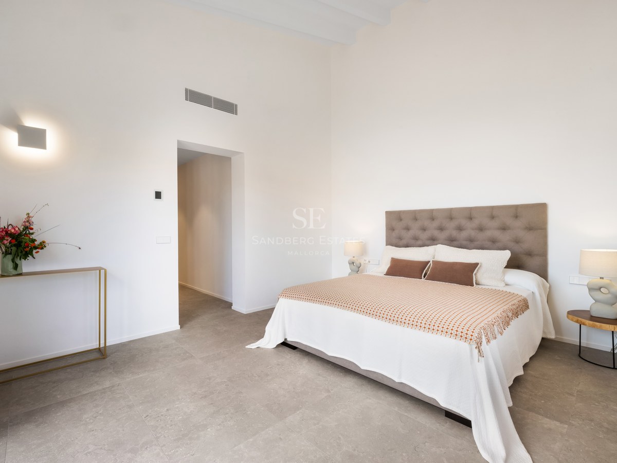 Minimalist bedroom with a tufted headboard, white bedding, designer lamps, and grey stone floors under high ceilings.