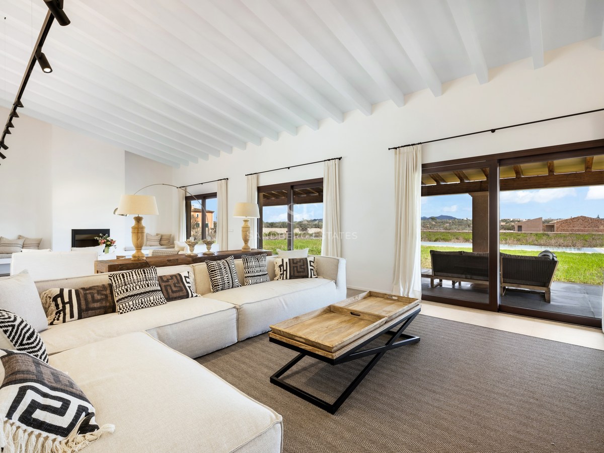 Bright living room with large L-shaped sofa, white wooden ceiling beams, and glass doors opening to a scenic terrace.