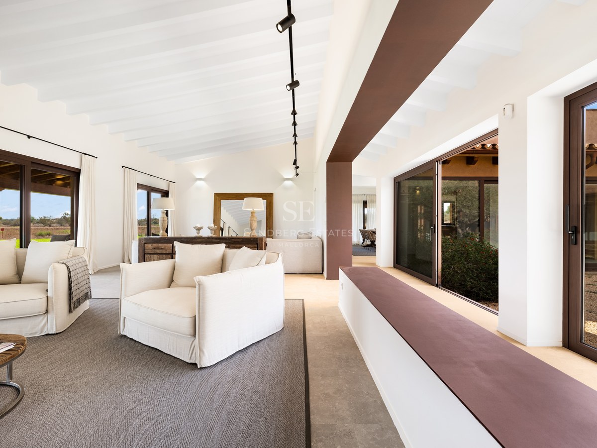 Spacious living room featuring white sofas, white beamed ceilings, and large glass doors opening to the outdoors.