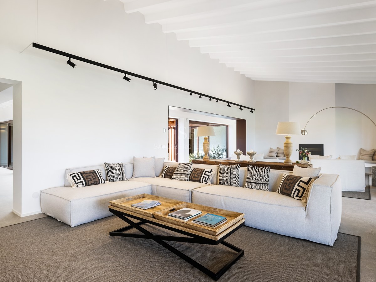 Spacious living room featuring a large grey sectional sofa, geometric cushions, and wooden coffee table under a white beamed ceiling.