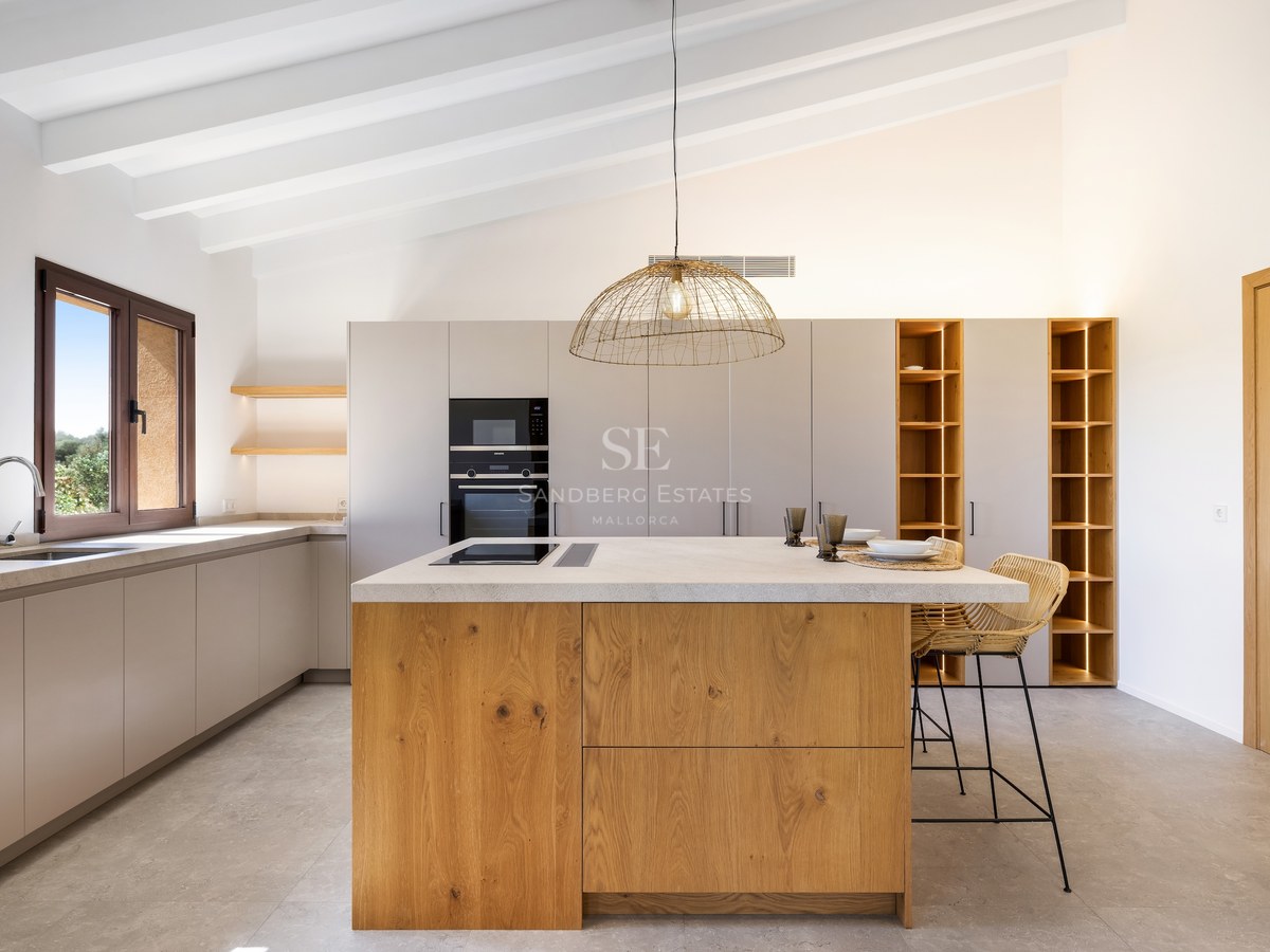 Bright kitchen featuring a large oak island, white beamed ceiling, and integrated lighting in open shelving.