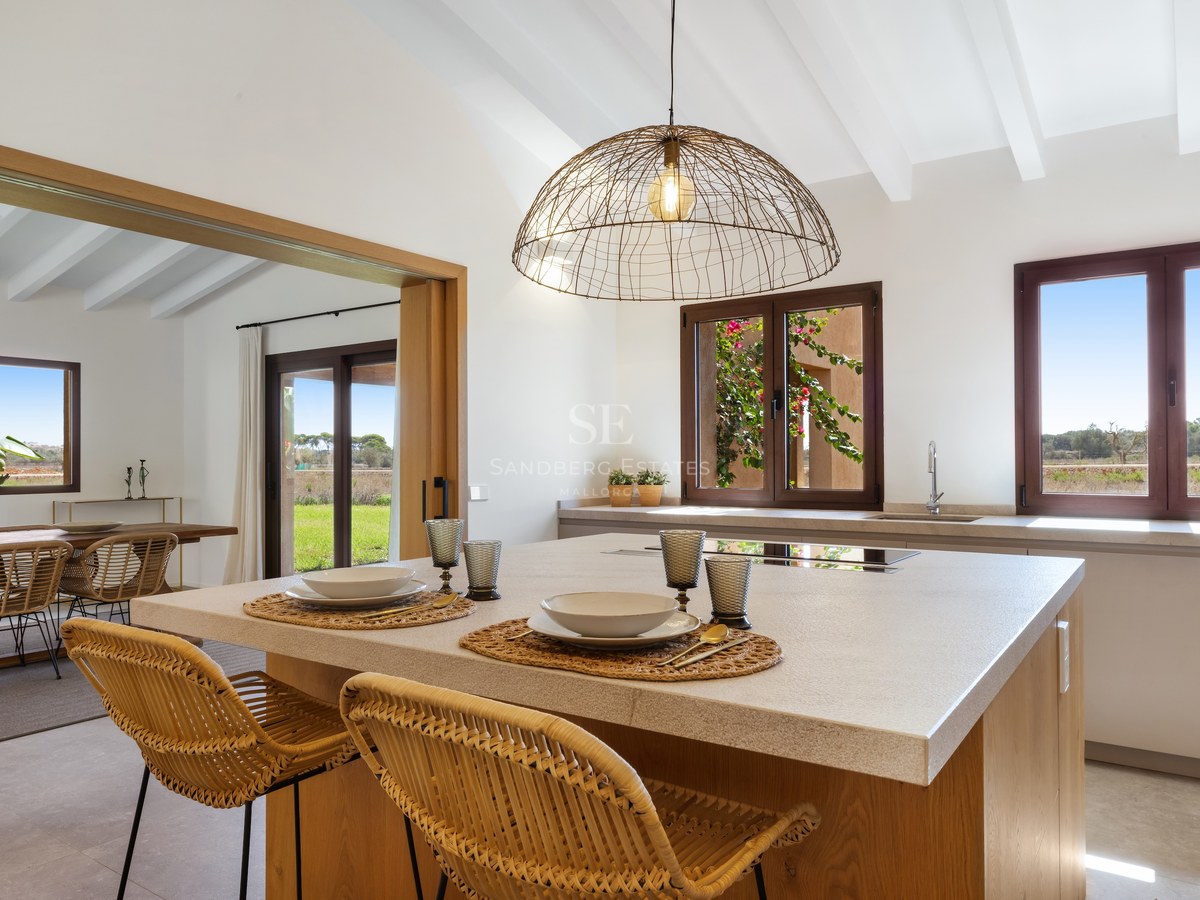 Modern kitchen island with wicker stools and white beamed ceiling overlooking rural landscape.