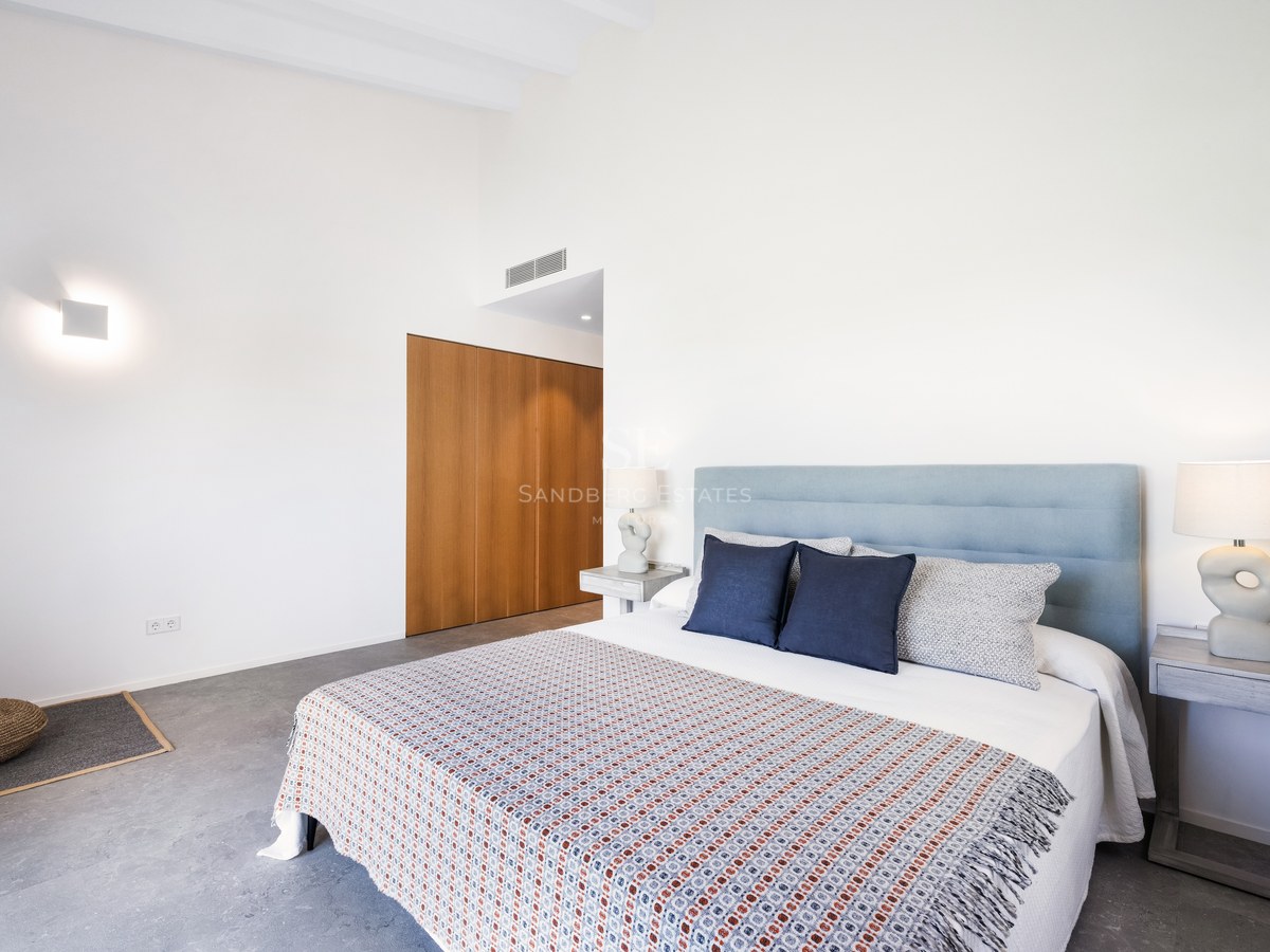 Bright bedroom with a large bed, light blue headboard, designer lamps, and built-in wooden wardrobe.