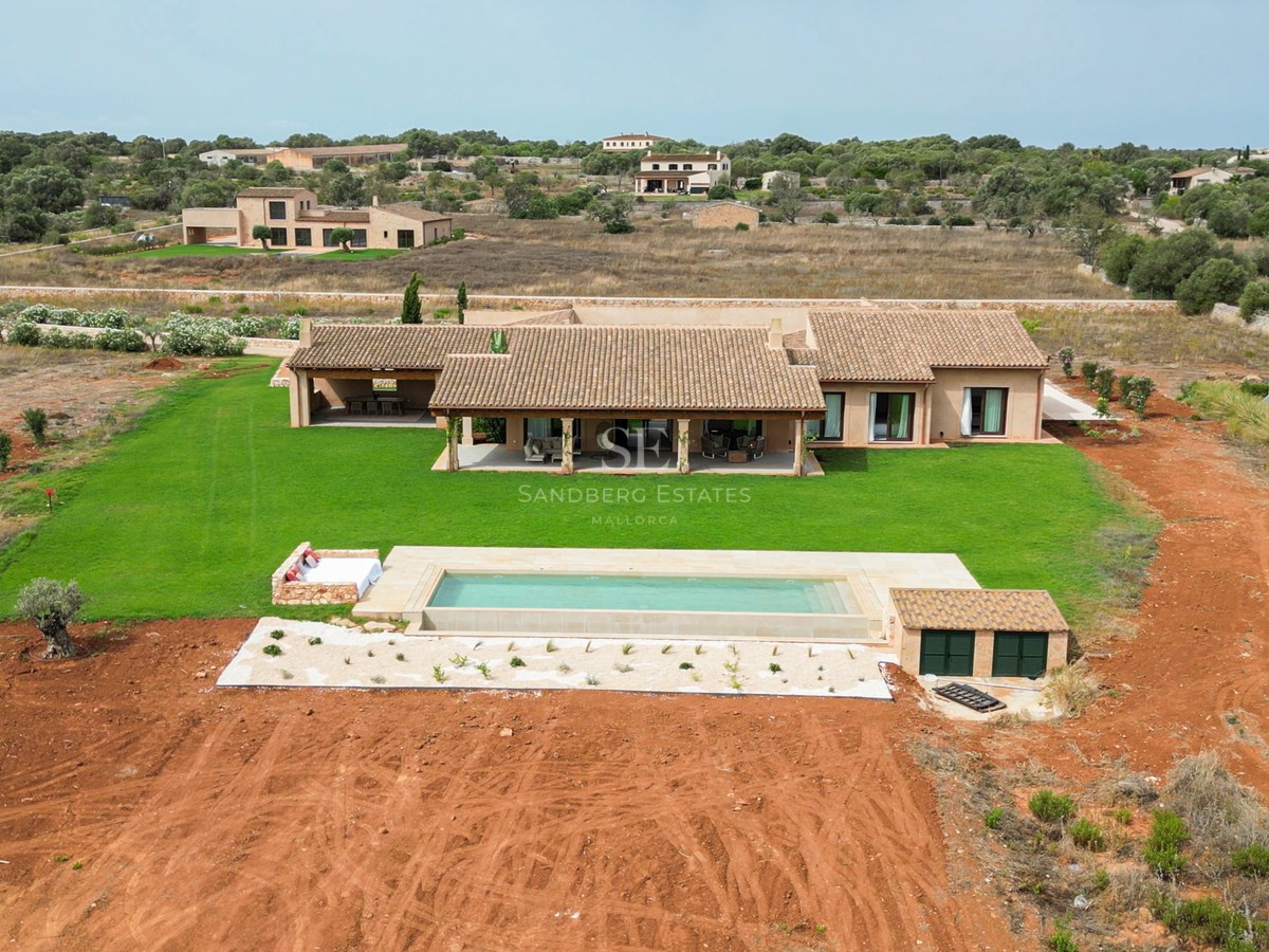 Bird's eye view of a luxury villa with terracotta roof, rectangular swimming pool, and large green lawn.