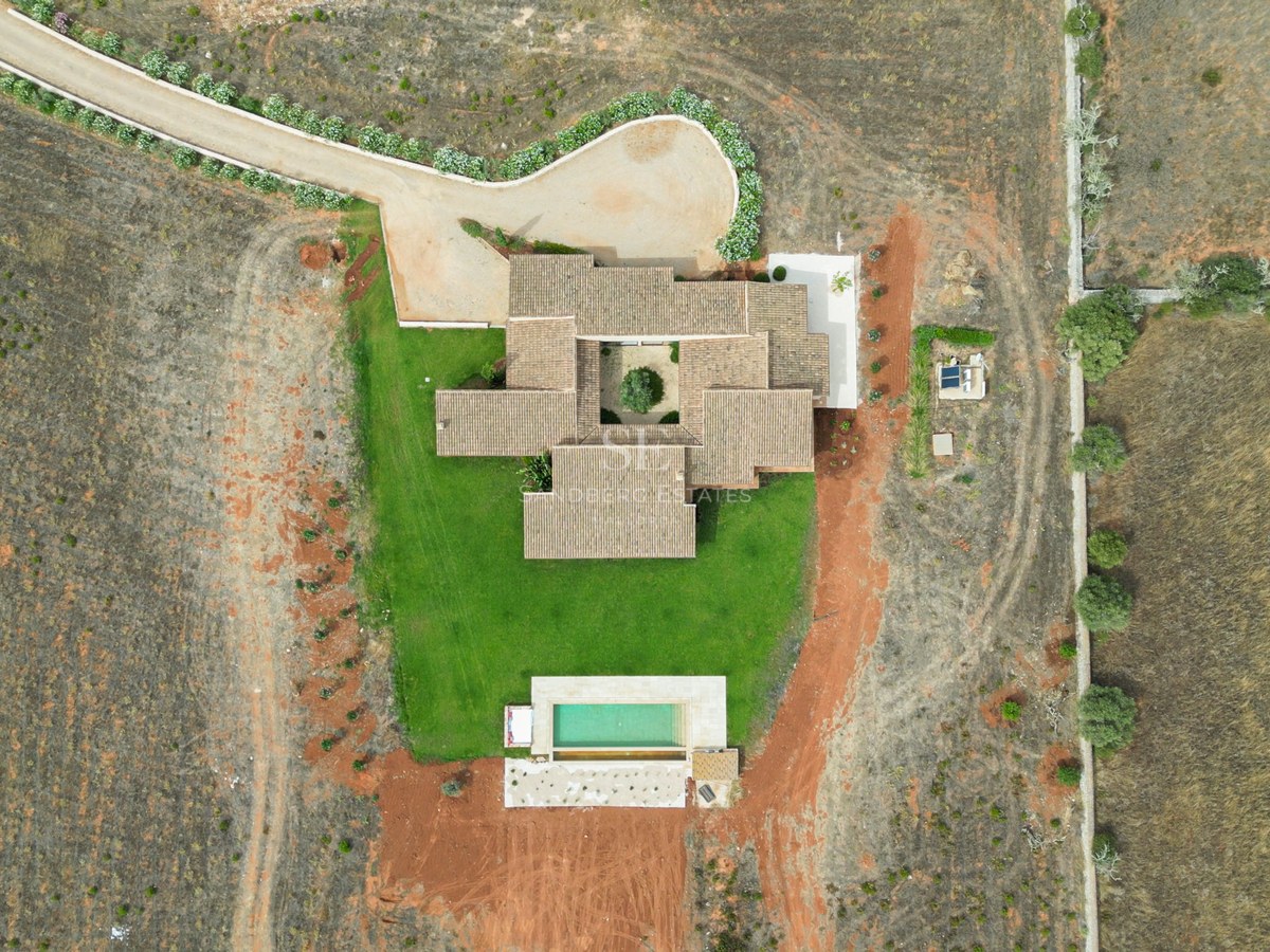 Top-down drone view of a tiled-roof villa with a central interior courtyard, lawn, and rectangular swimming pool.